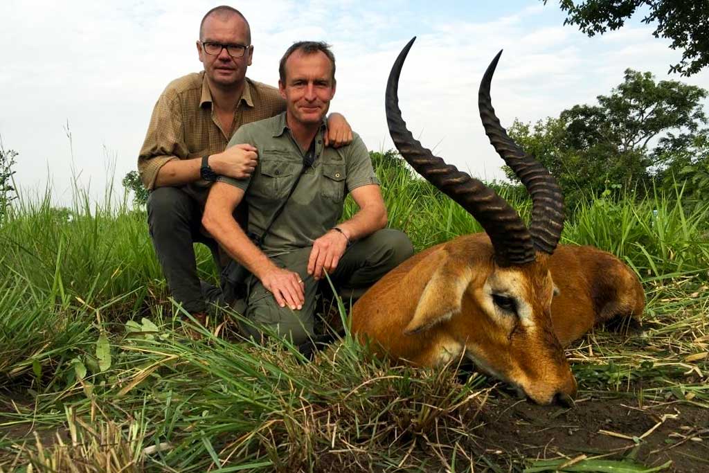 Guests pose for a photo moment besides a waterbuck while on a ssport hunting safari in Lake Mburo National Park.